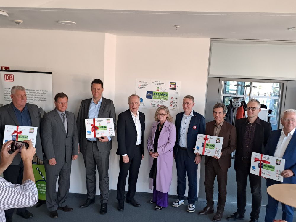 Acht Männer und eine Frau posieren für ein Pressefoto. VIer Männer halten je ien Schilz mit der Aufschrift "Allianz Siemensbahn" in der Hand.