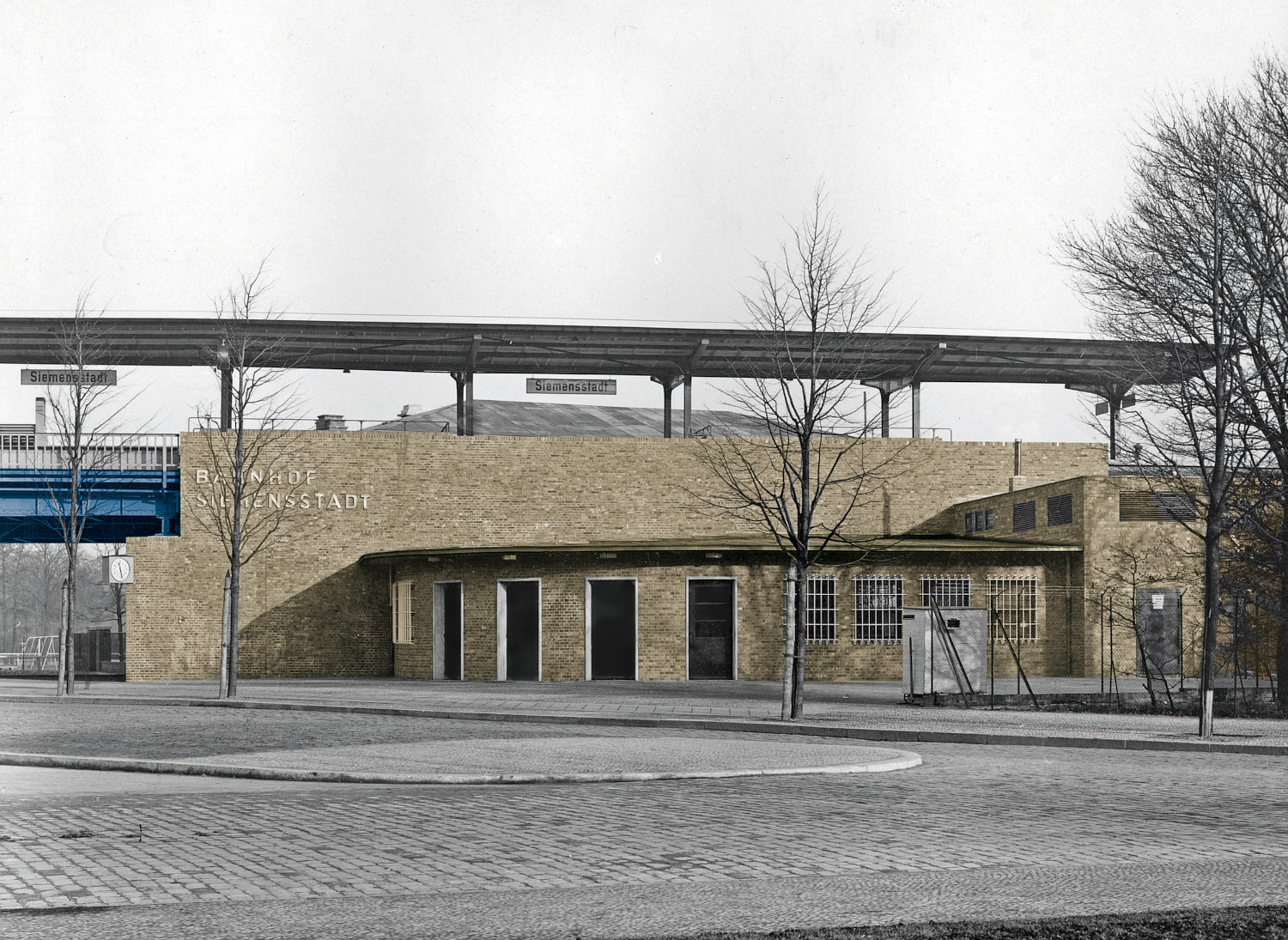 Archiv-Foto (Schwarz-weiß) des Bahnhofs Siemensstadt, Empfangsgebäude und Stahlviadukt eingefärbt